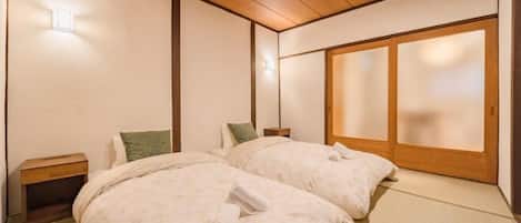 Ein traditioneller japanischer Raum mit Tatami-Boden, zwei Betten mit ordentlich gefalteten Handtüchern, einer Holzbalkendecke und Schiebetüren.