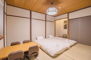 A traditional Japanese-style room with tatami flooring, a low wooden table with chairs, a bed with white bedding, and a hanging light fixture. - FOXINN (Osaka)