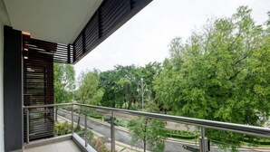 Een balkon met een metalen hekwerk, uitkijkend op een weg en groen.