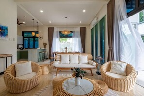 A modern living room with a sofa, two wicker chairs, a coffee table, and a kitchen in the background. - Bungalow Putrajaya 15Pax w Private Pool Gathering (Putrajaya)