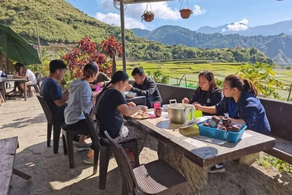 A group of people dining outdoors with a scenic view of mountains and fields.