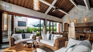 A modern living room with wicker furniture, a wooden coffee table, and large windows offering a view of greenery. - Villa Zen Paradise by BaliSuperHost (Bali)