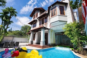 Une maison à deux étages avec une piscine, un espace salon extérieur et un jardin.