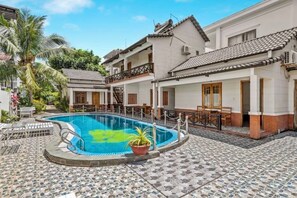 A swimming pool surrounded by a tiled patio with a white building and a palm tree. - Nhat Huy Bungalow Phu Quoc (Phu Quoc Island)