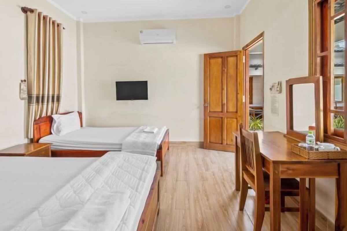 Een hotelkamer met twee bedden, een houten bureau, een stoel, een televisie en een kledingkast.