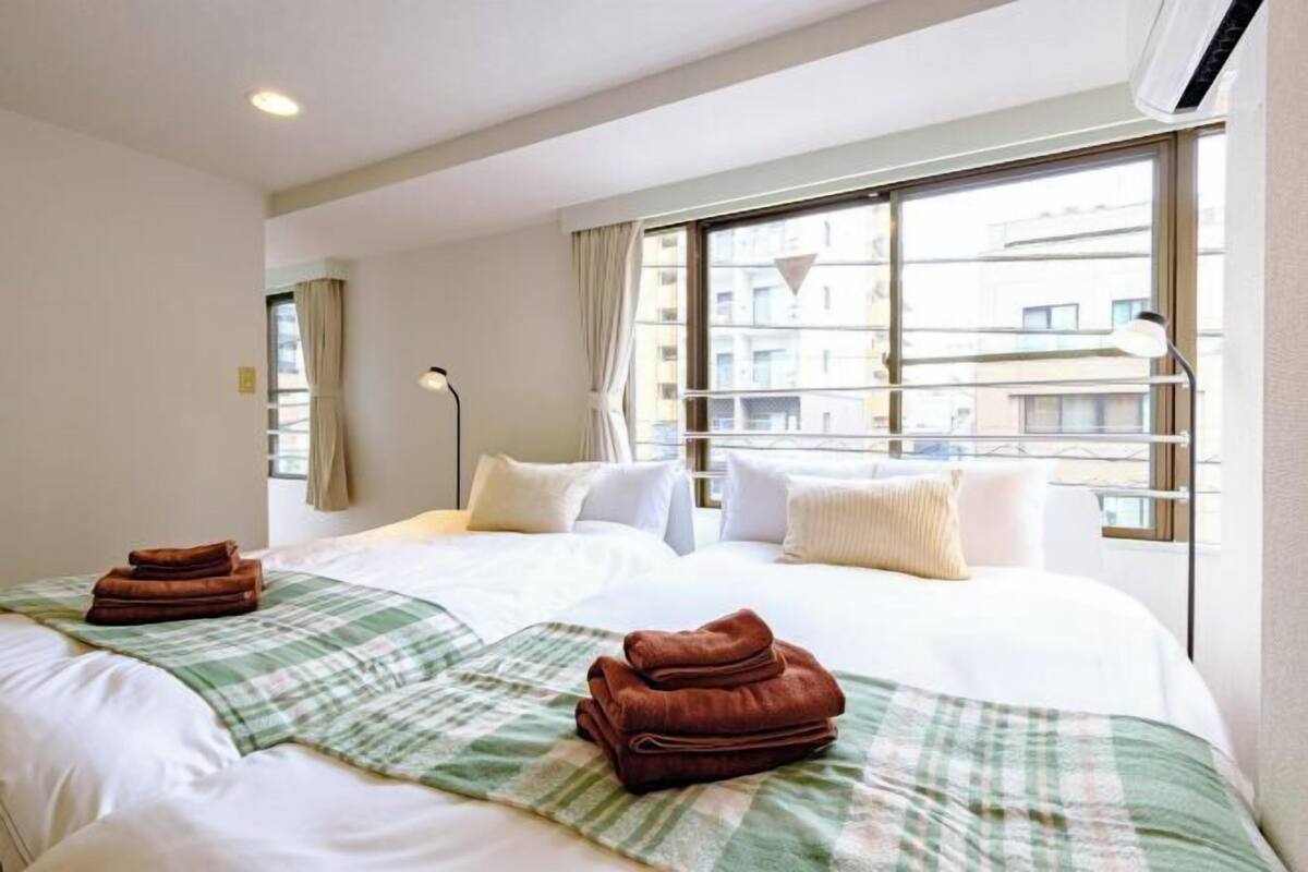 A hotel room with two beds, a large window, and a view of buildings.