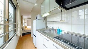 A modern kitchen with white cabinets, a stainless steel countertop, and a built-in microwave. - Land Forest Ryogoku (Tokyo)