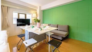 A modern living room with a green accent wall, a sofa, a dining table with chairs, a TV, and a window with curtains. - Land Forest Ryogoku (Tokyo)