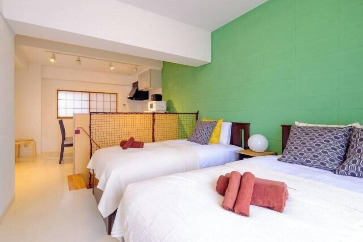 A hotel room with two beds, a green accent wall, and a kitchenette.