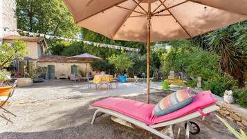 Une terrasse avec un fauteuil de relaxation, une table et un parasol suspendu.