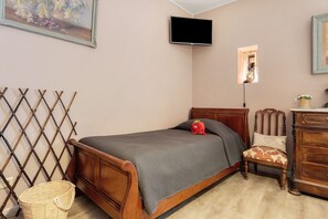 Un dormitorio con una cama de madera, un televisor montado en la pared, una ventana pequeña con un adorno de mariposa y una cesta de mimbre.