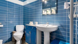 Et badeværelse med blå fliser, et hvidt toilet, en vask og et spejl.