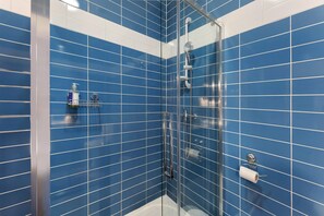 A bathroom with blue tiled walls, a glass shower enclosure, and a toilet paper holder. - Guest Room 'Family Suite Guy De Maupassant' with Shared Terrace, Wi-Fi and Air Conditioning (Bernis)