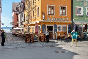 A street with outdoor seating, a restaurant named 'Ins Fischerntz,' and a hotel with signage.