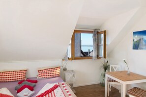 A bedroom with a bed, a desk, a chair, a window with curtains, and a plant.