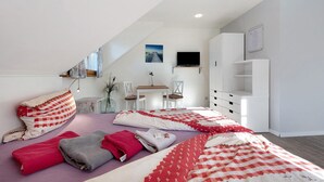 Un dormitorio con techo inclinado, una cama con varias mantas, un televisor, un escritorio y una silla.
