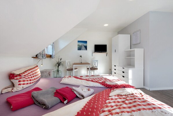 A bedroom with a sloped ceiling, a bed with multiple blankets, a TV, a desk, and a chair.