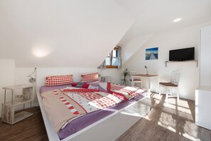 A bedroom with a bed, a desk, a chair, a TV, and a window.