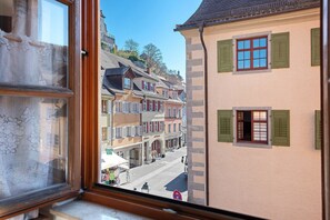 A view through a window of a street with buildings, including a building with green shutters and a sign that reads 'Hotel.'