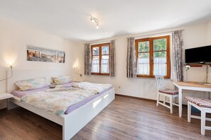A bedroom with a bed, a desk, a chair, a TV, and a painting on the wall.