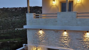 A modern two-story building with stone walls and a wooden deck. There are two outdoor seating areas with chairs and a hot tub. - Amvikas Suites in Sitia (Sitia)