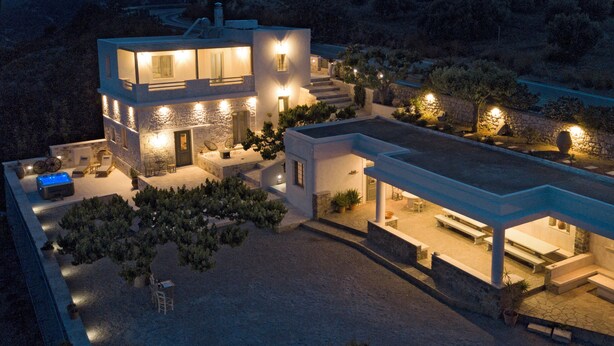 A modern two-story house with a stone facade, outdoor seating, and a well-lit patio area. - Amvikas Suites in Sitia (Sitia)