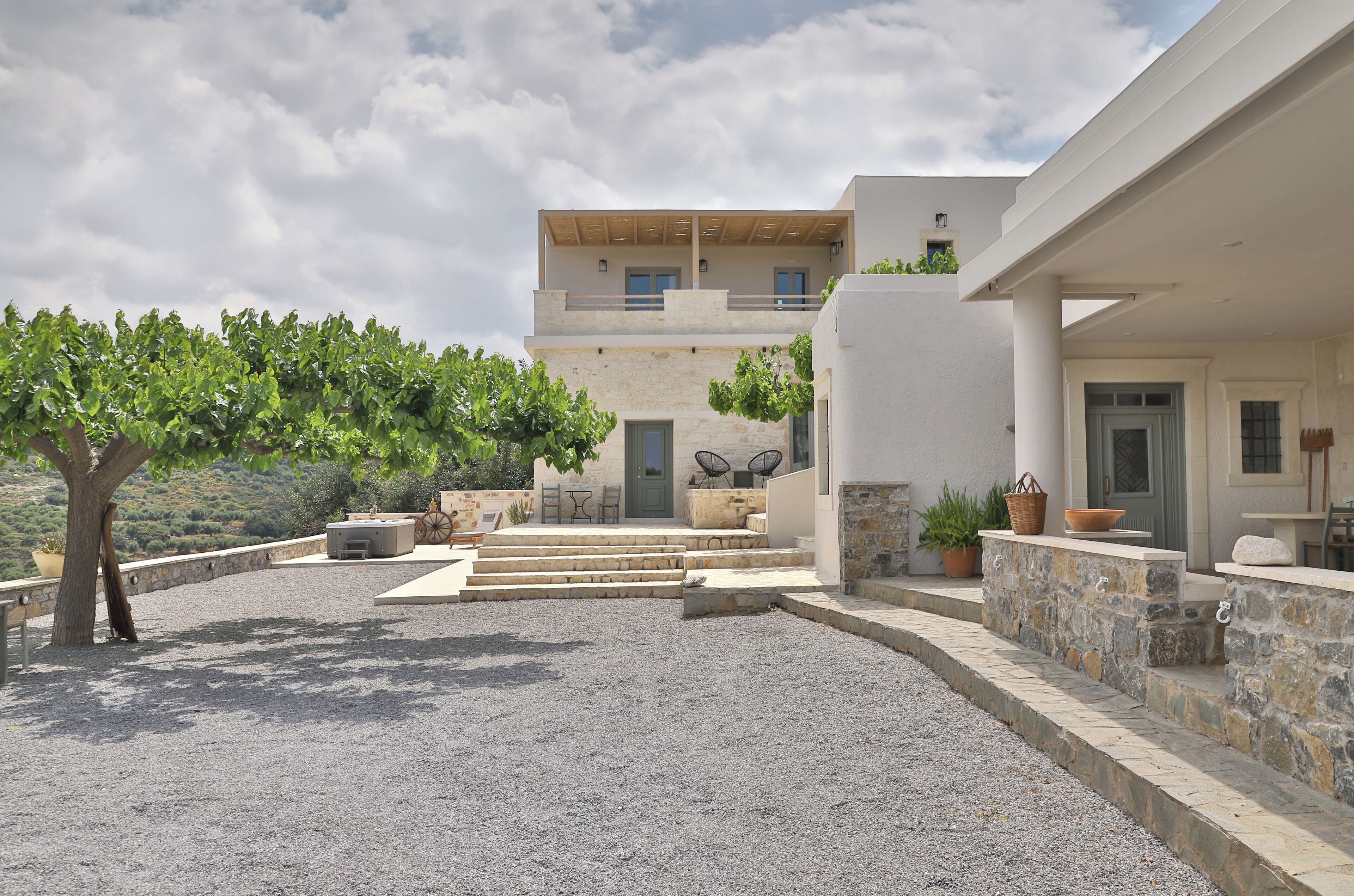 A modern villa with a stone facade, a covered outdoor seating area, and a view of the surrounding landscape.