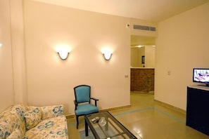 Un hall d’hôtel avec un canapé, un fauteuil, une table basse en verre, un téléviseur et des lampes fixées au mur.