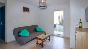 Ein Wohnzimmer mit grauem Sofa, türkisfarbenen Kissen, einem Holztisch und einer Tür, die nach draußen führt.