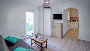 Ein Wohnzimmer mit einer Couch, einem Couchtisch und einem an der Wand befestigten Fernseher. Eine Tür führt zu einem Balkon.
