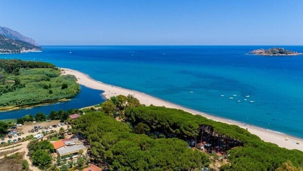 Une zone côtière comprenant une plage, une petite île et un espace de stationnement avec des bâtiments.