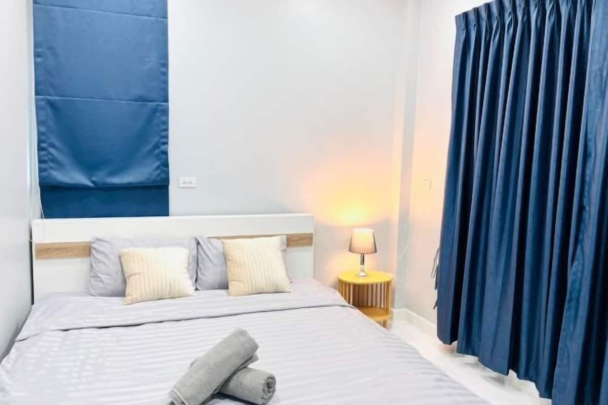 Una camera d'hotel con un letto, cuscini, un comodino con una lampada e tende blu.