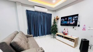 A modern living room with a grey sofa, a television mounted on the wall, a small Christmas tree, and a wooden console table. - Chiang Khan Kor Pool Villa (Chiang Khan)