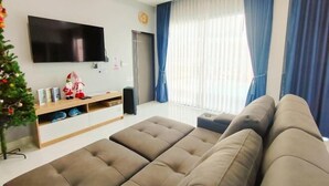 A modern living room with a large flat-screen TV, a sofa, a small ottoman, and a Christmas tree. - Chiang Khan Kor Pool Villa (Chiang Khan)