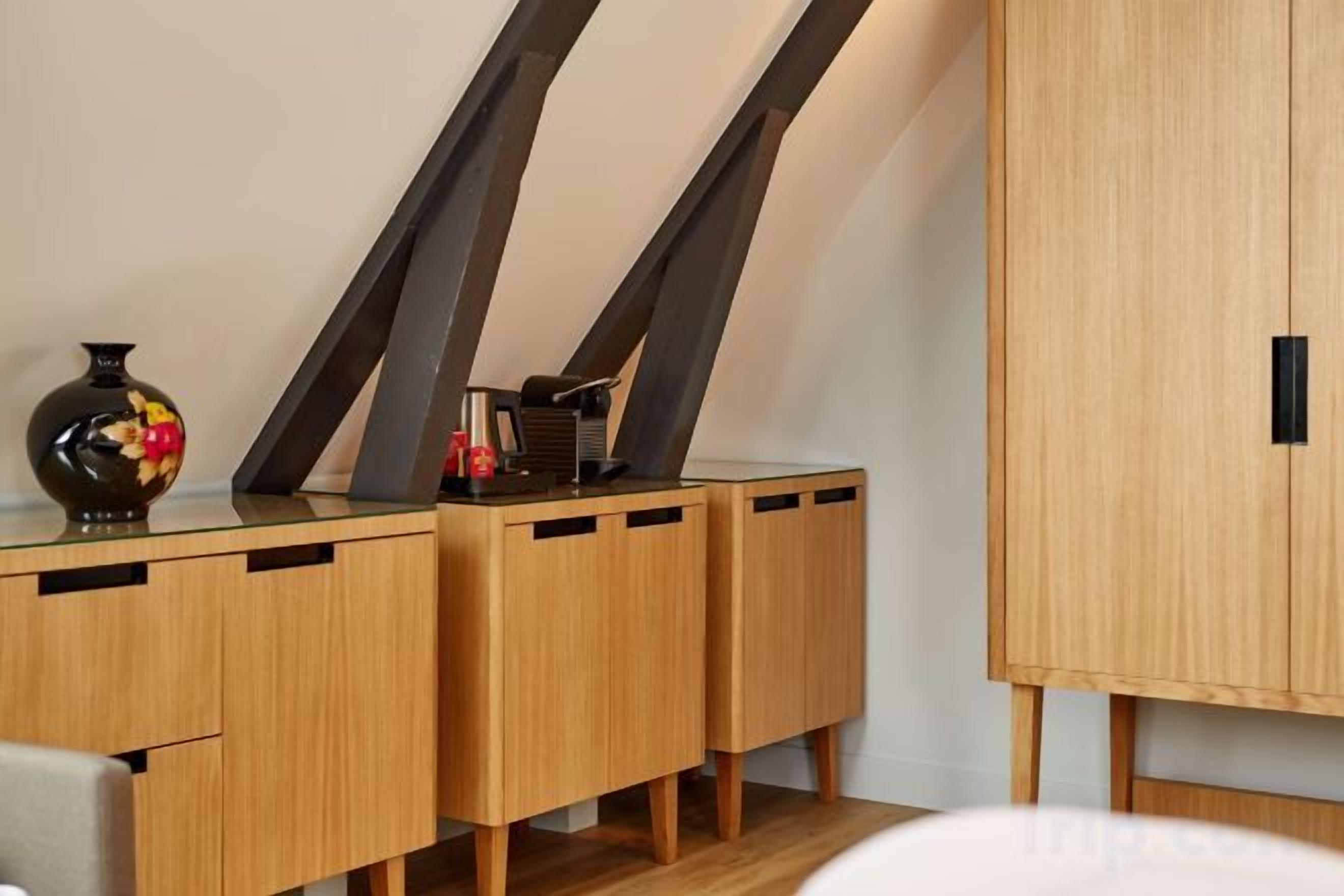 Een hoek van een kamer met een houten kast, een vaas met bloemen en een zwart voorwerp op de kast.