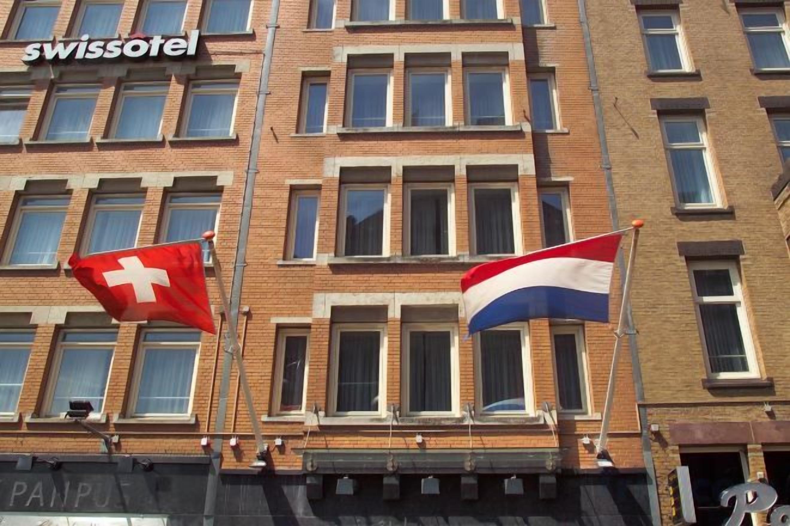 Een gebouw met veel ramen en vlaggen, waaronder een Zwitserse vlag en een vlag met horizontale strepen.