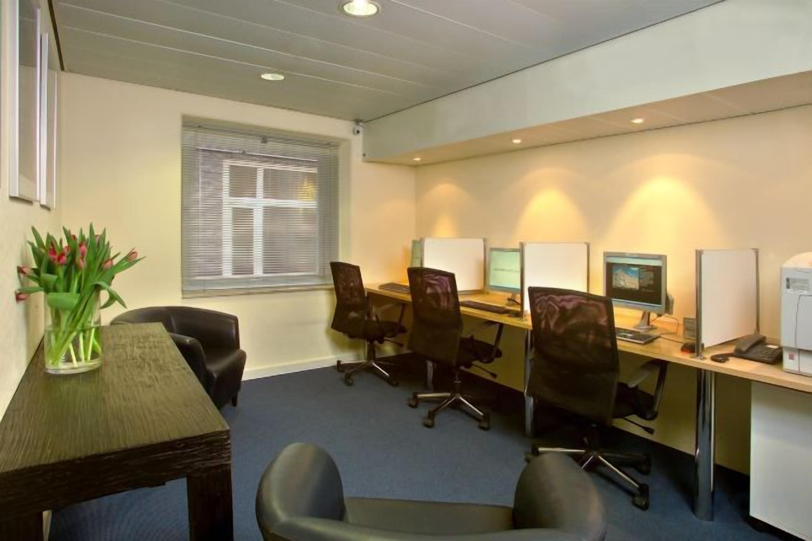 Een vergaderruimte met een lange tafel, diverse stoelen, een computer en een printer.