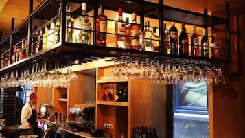 Een bar met flessen en glazen op de planken, een barman en een raam met uitzicht.