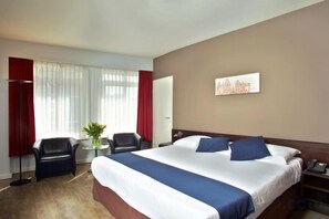 A hotel room with a large bed, two chairs, a desk, and a window with curtains. - Swissôtel Amsterdam (Amsterdam)