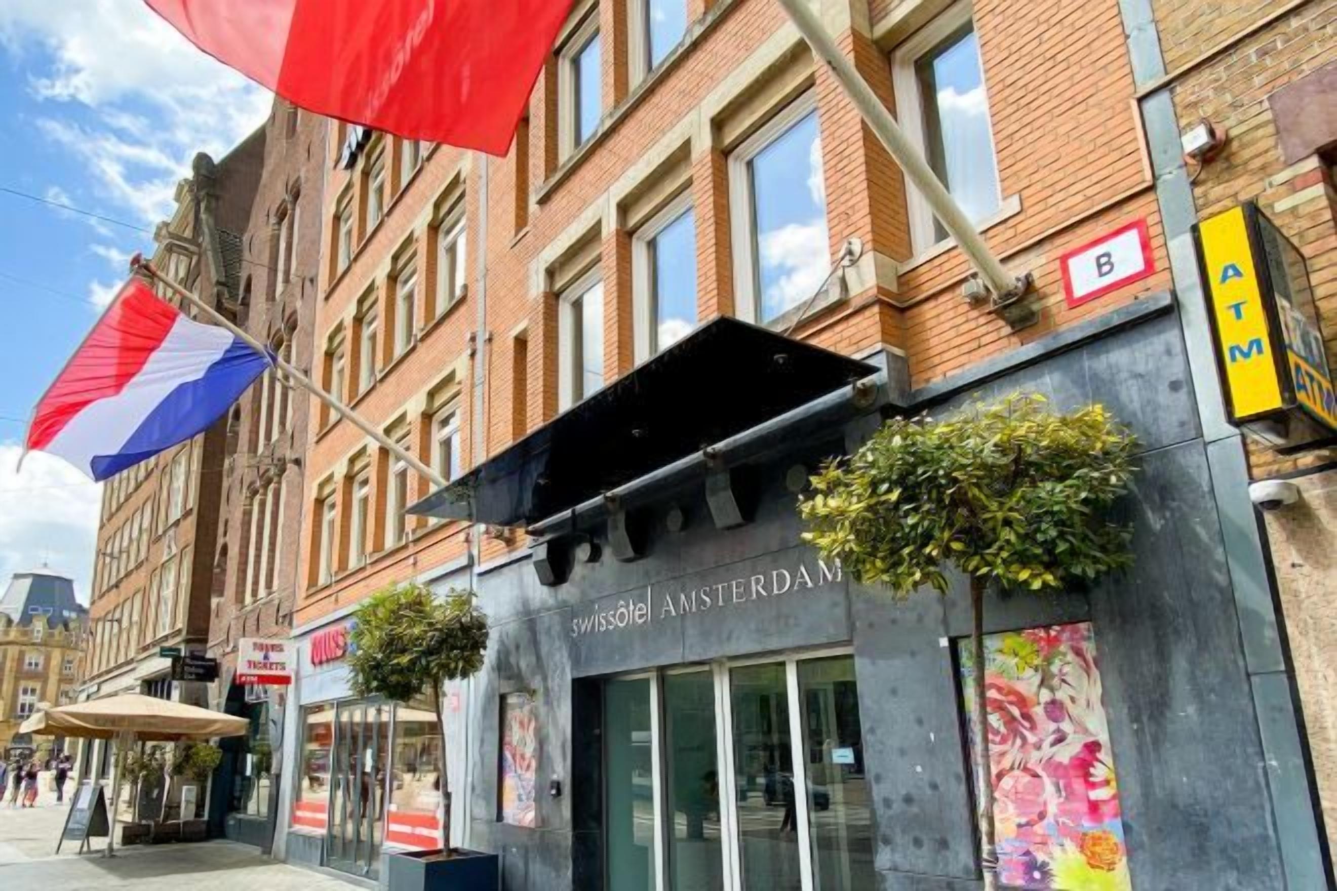 Een hotel met een bord waarop 'swissôtel AMSTERDAM' staat en een zichtbare geldautomaat aan de rechterkant.