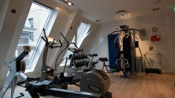 Un gimnasio con máquinas de cardio, una banca de pesas y un estante de pared.