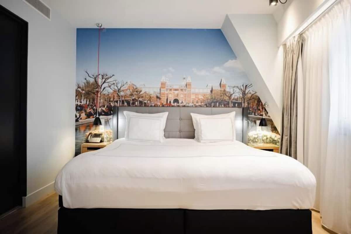 A bedroom with a large bed, two bedside tables, and a mural of a historic building on the wall.