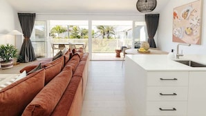 A modern kitchen with a white countertop, a built-in sink, and a dining area with a brown sofa and a table. - Villa Palmera by Balmy Breaks - 100m to Beach (Noosa)