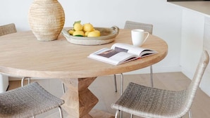 A round wooden table with a woven chair, a woven vase, a bowl of lemons, a white cup, and an open magazine. - Villa Palmera by Balmy Breaks - 100m to Beach (Noosa)