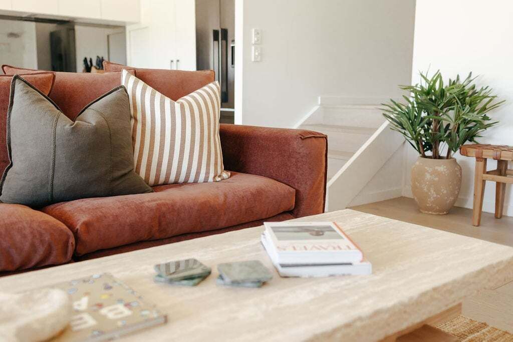 Una sala de estar con un sofá de cuero marrón, un cojín a rayas y una mesa de centro con libros y objetos decorativos.
