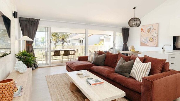 A modern living room with a brown sofa, a wooden coffee table, and a large sliding glass door leading to an outdoor patio. - Villa Palmera by Balmy Breaks - 100m to Beach (Noosa)