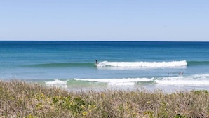 A beach with clear blue water and waves, and people swimming and surfing. - Villa Palmera by Balmy Breaks - 100m to Beach (Noosa)