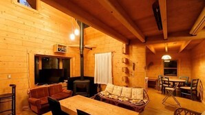 A wooden cabin interior with a sofa, table, chairs, a fireplace, and a television. - Log House Nasu High Grand (Nasu)
