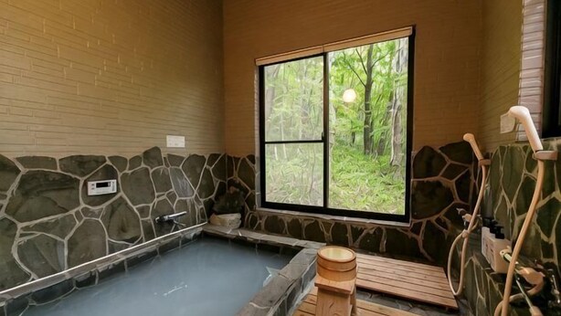 A stone-walled room with a wooden bathtub, a window with a view of greenery, and a wooden bench. - Log House Nasu High Grand (Nasu)
