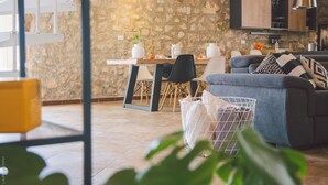Una sala de estar moderna con una pared de piedra, un comedor con mesa y sillas, y un sofá gris con cojines estampados.